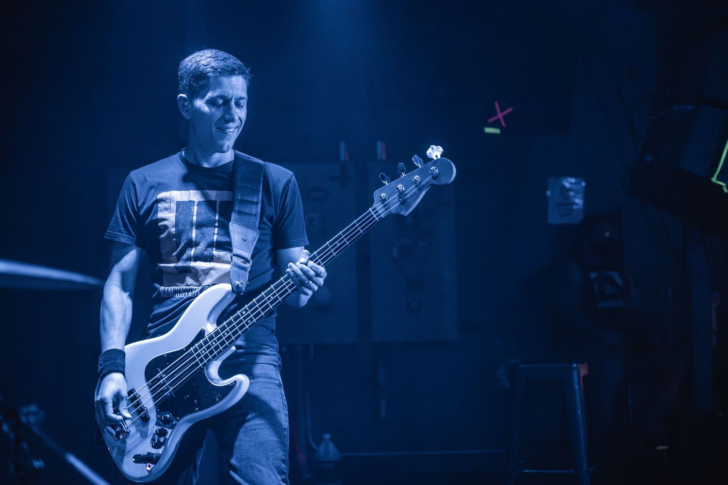 Bassist plays electric bass guitar on dimly lit stage with blue lighting effects.