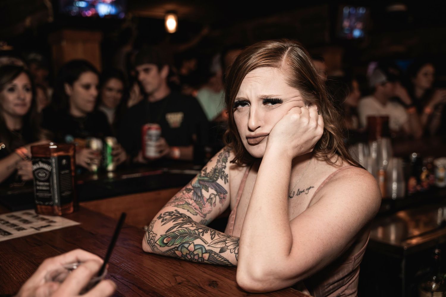 Person with tattoos sitting at a dimly lit bar counter.