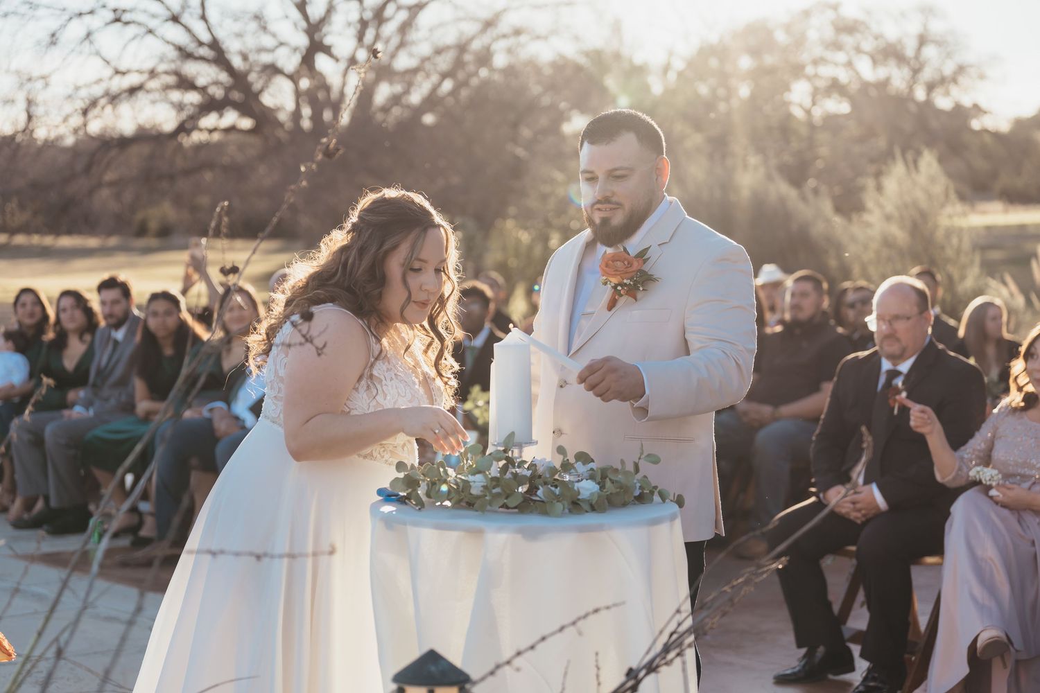 Outdoor wedding ceremony moment with guests watching in background during sunset.