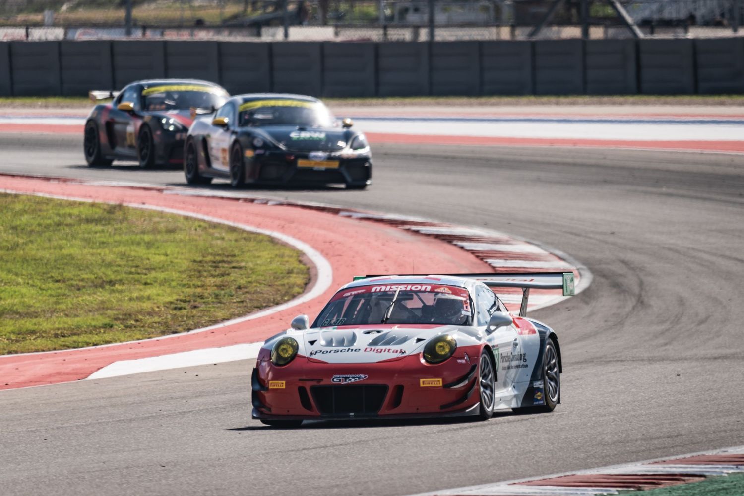 Porsche GT3 race car leads competitors through a sweeping racetrack turn.