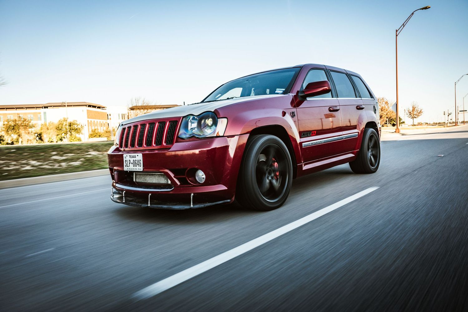 Modified maroon Jeep Grand Cherokee SRT photographed in motion on urban road.