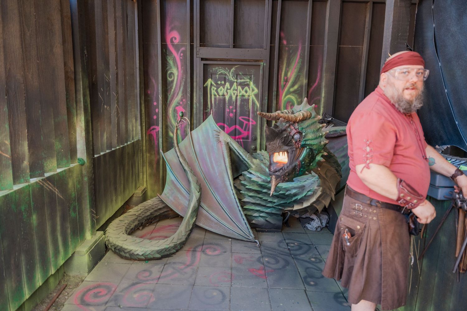 Artisan demonstrating metalworking skills near a decorative dragon prop at a medieval fair.