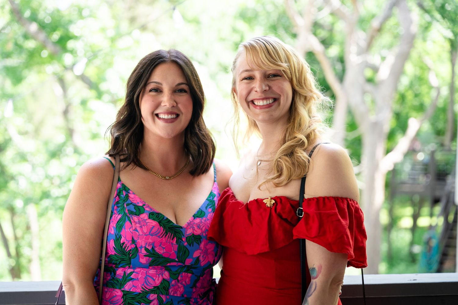 Two guests in festive dresses smile at an outdoor summer wedding.