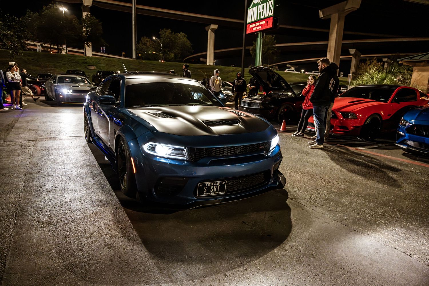 Blue Dodge Charger with glowing headlights at nighttime car meet.