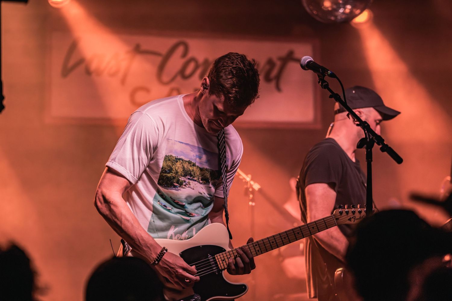 Guitarist focuses intently on playing during a performance under warm red stage lighting.