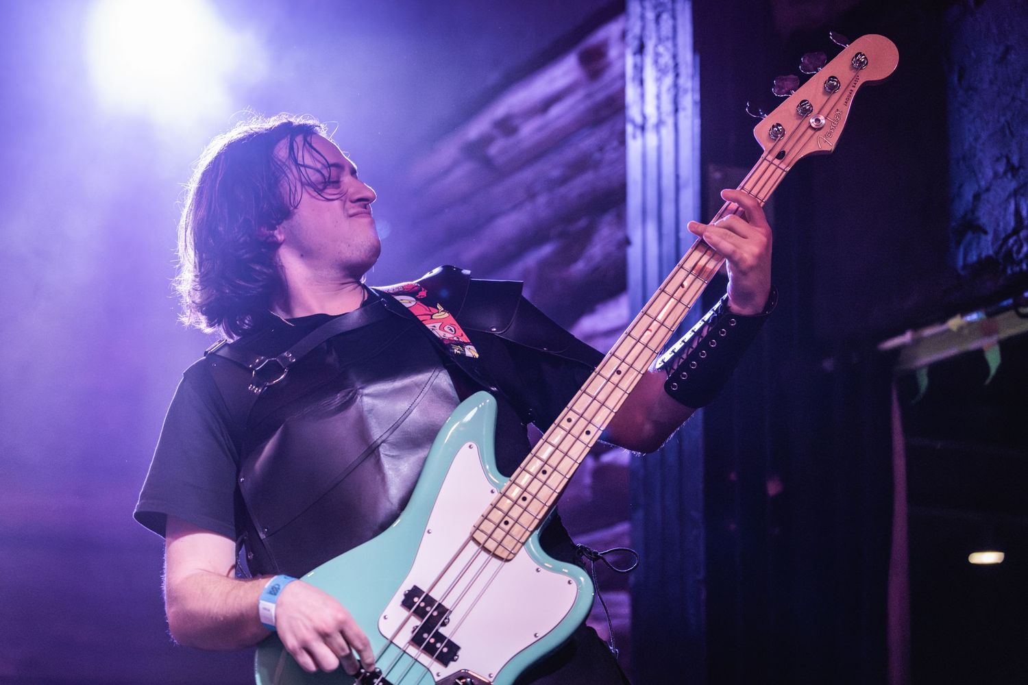 Bass guitarist plays passionately under purple stage lighting during live performance.