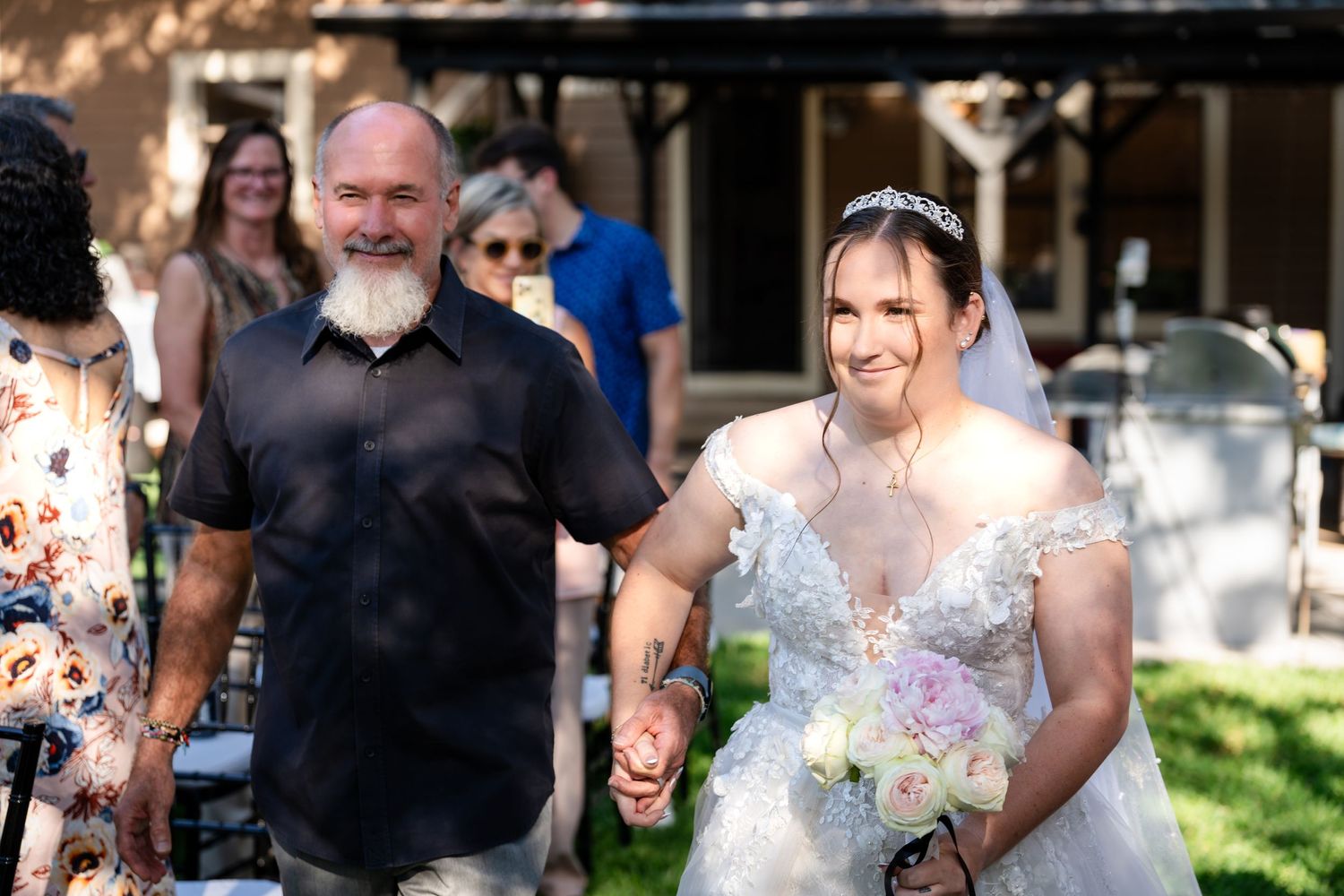 People gather outdoors for a wedding celebration on a sunny day.