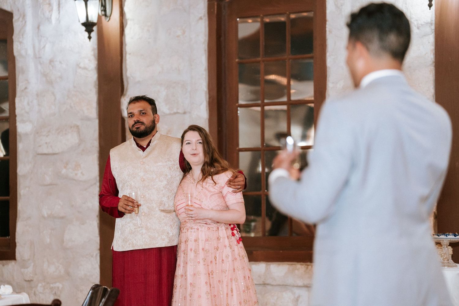 Wedding celebration attendees pose for photos in a rustic venue with stone walls.
