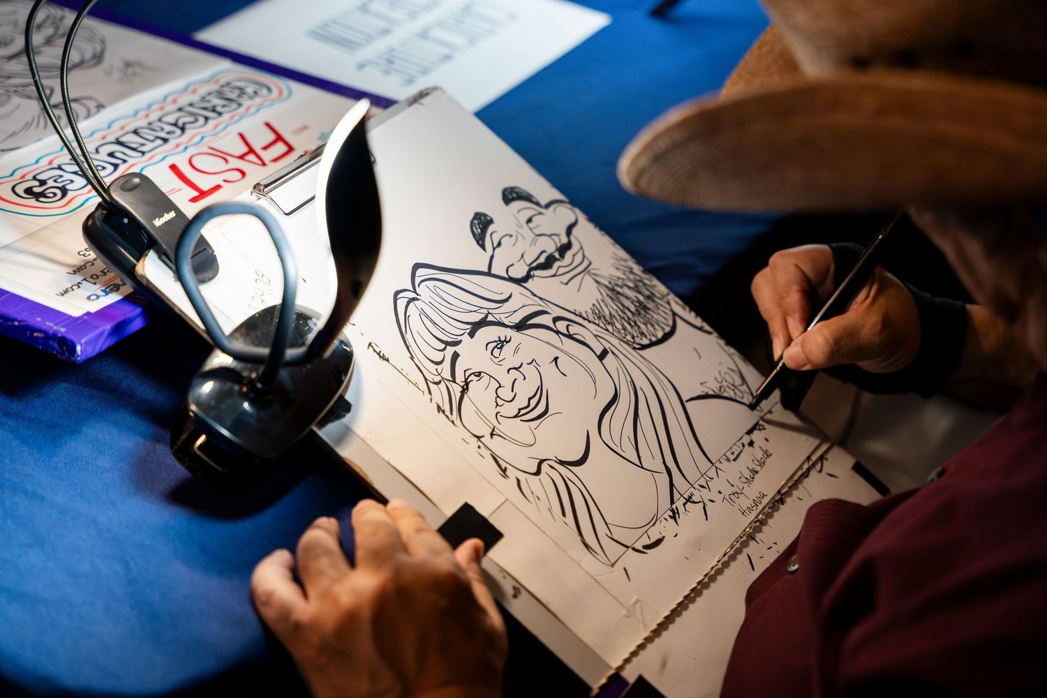 Artist works on a cartoon illustration at a drawing table with headphones and art supplies nearby.