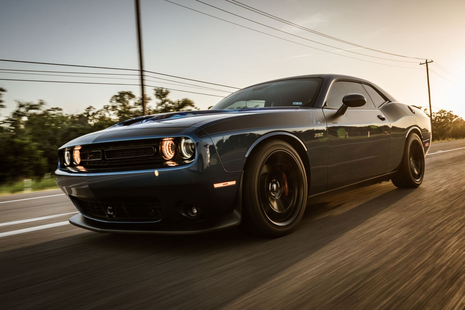 Black Dodge Challenger with orange accent lights photographed in motion during golden hour.