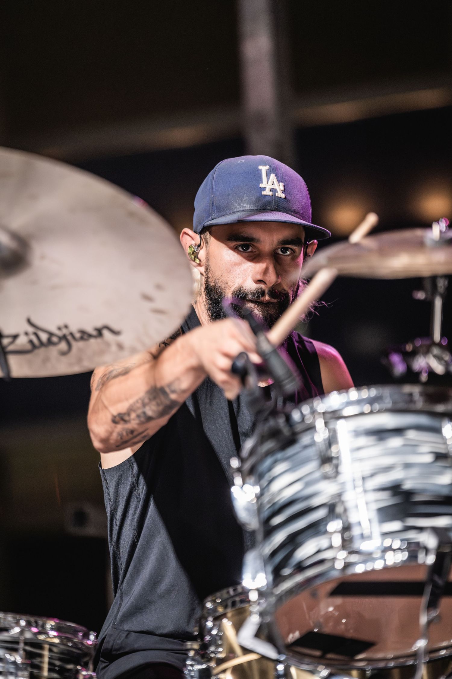 Drummer wearing LA baseball cap performing with intensity on stage.