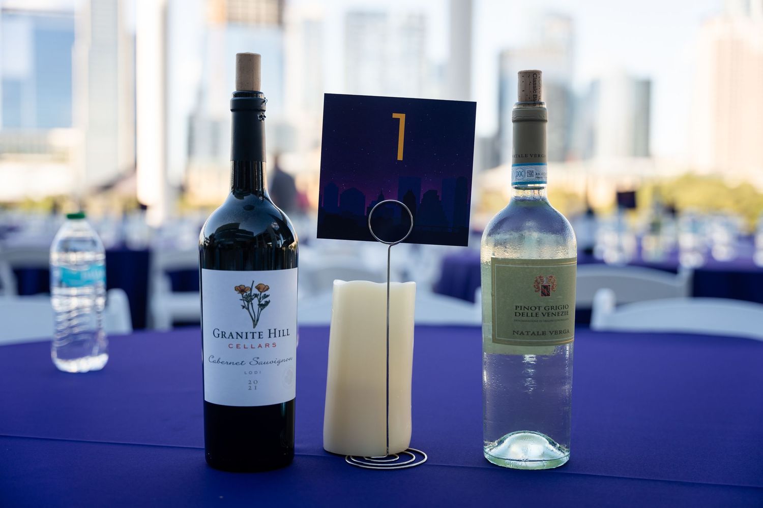 Wine bottles and table number on a dark blue tablecloth at an event setting.