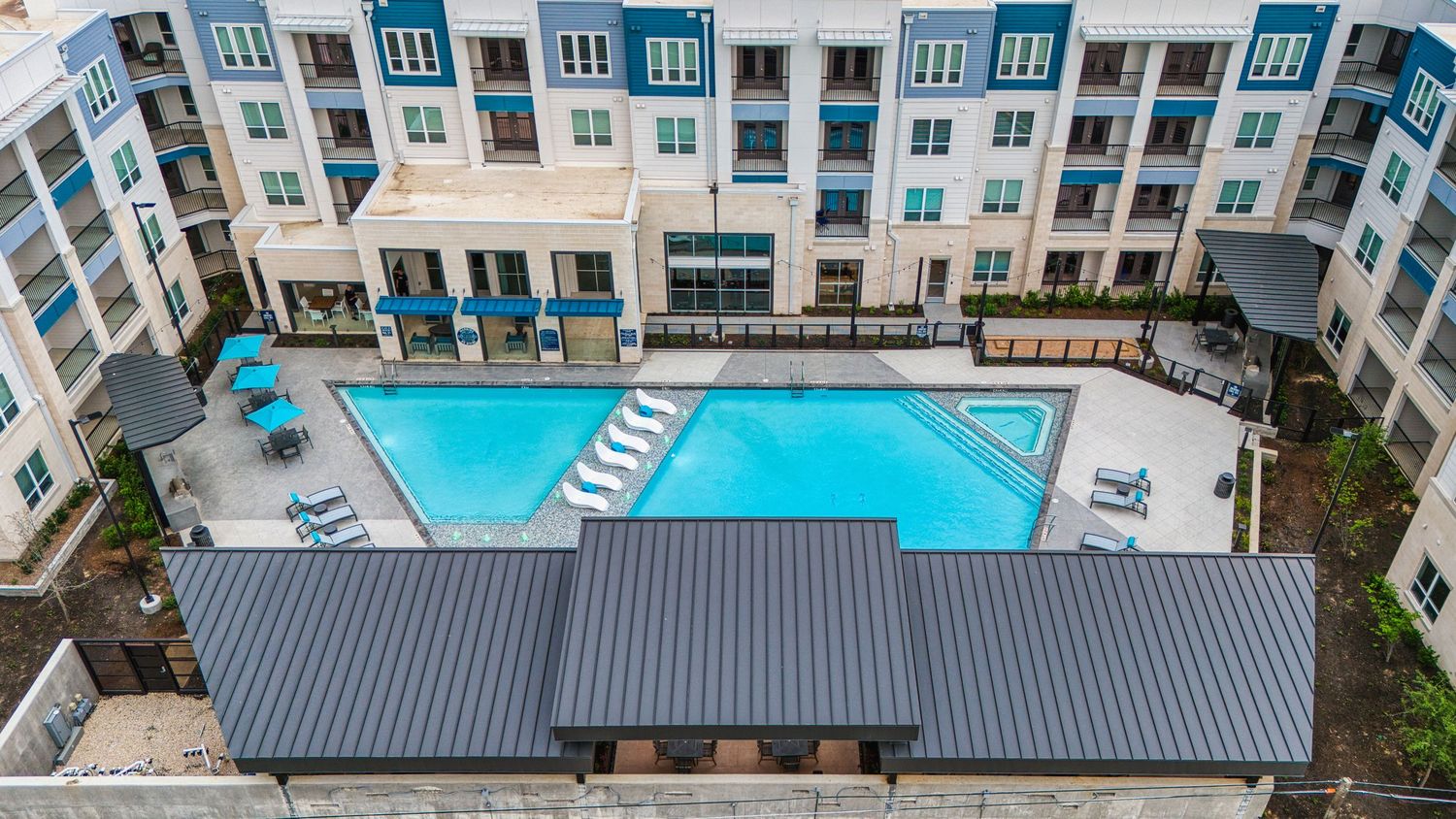 Aerial view of modern apartment complex with rectangular swimming pool and covered seating area.
