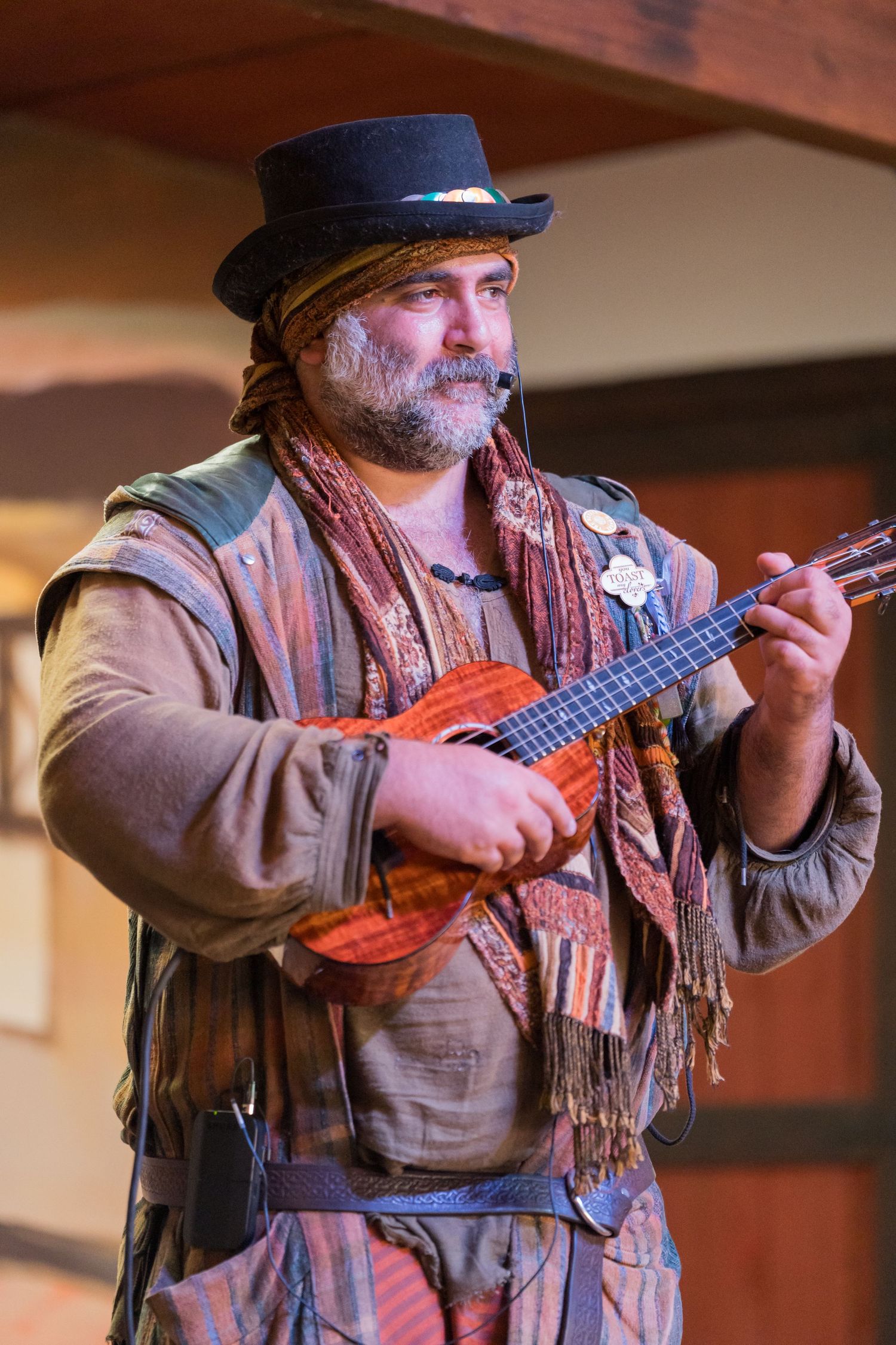 A performer in period costume plays a small stringed instrument on stage.