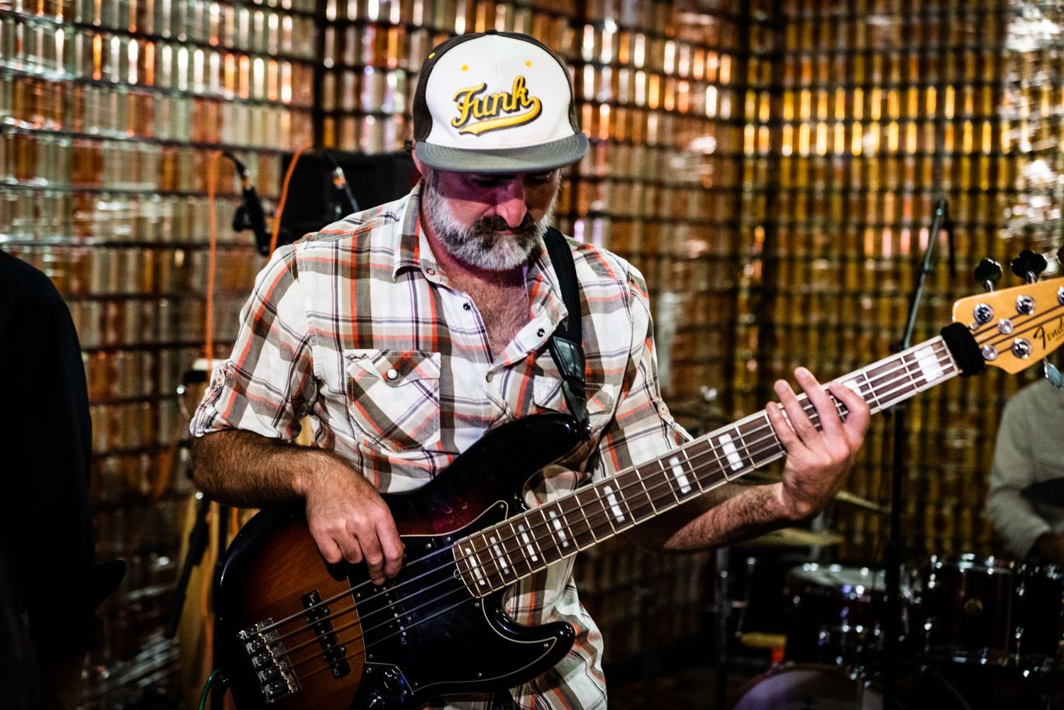 Bass player wearing plaid shirt and baseball cap performs on stage.