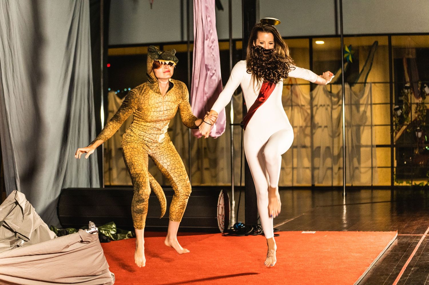 Two performers in contrasting gold and white costumes dance together on red stage floor.