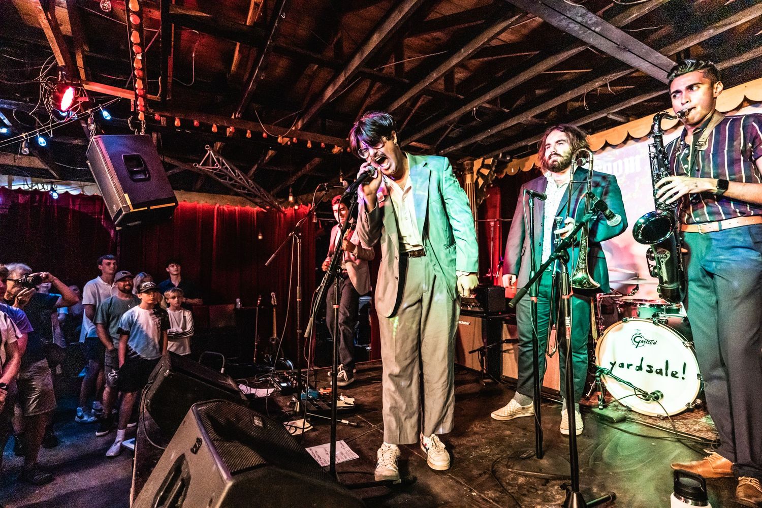 Musicians performing on stage in bright mint green suits at a crowded indoor venue.