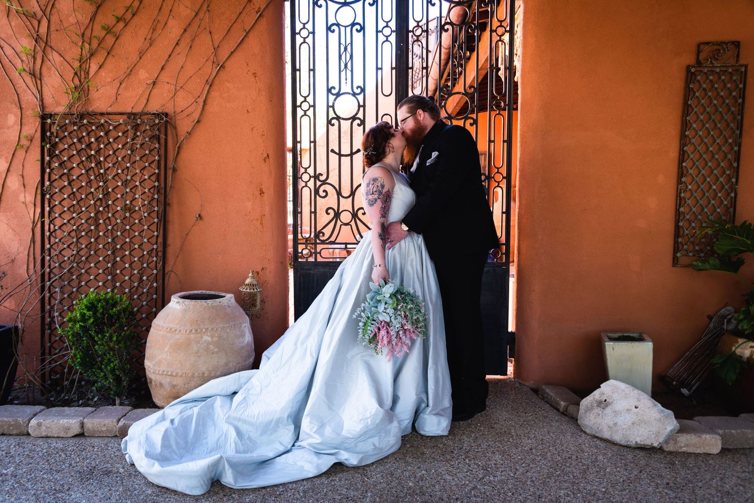 Wedding couple embraces by decorative gate with terracotta walls and pottery.