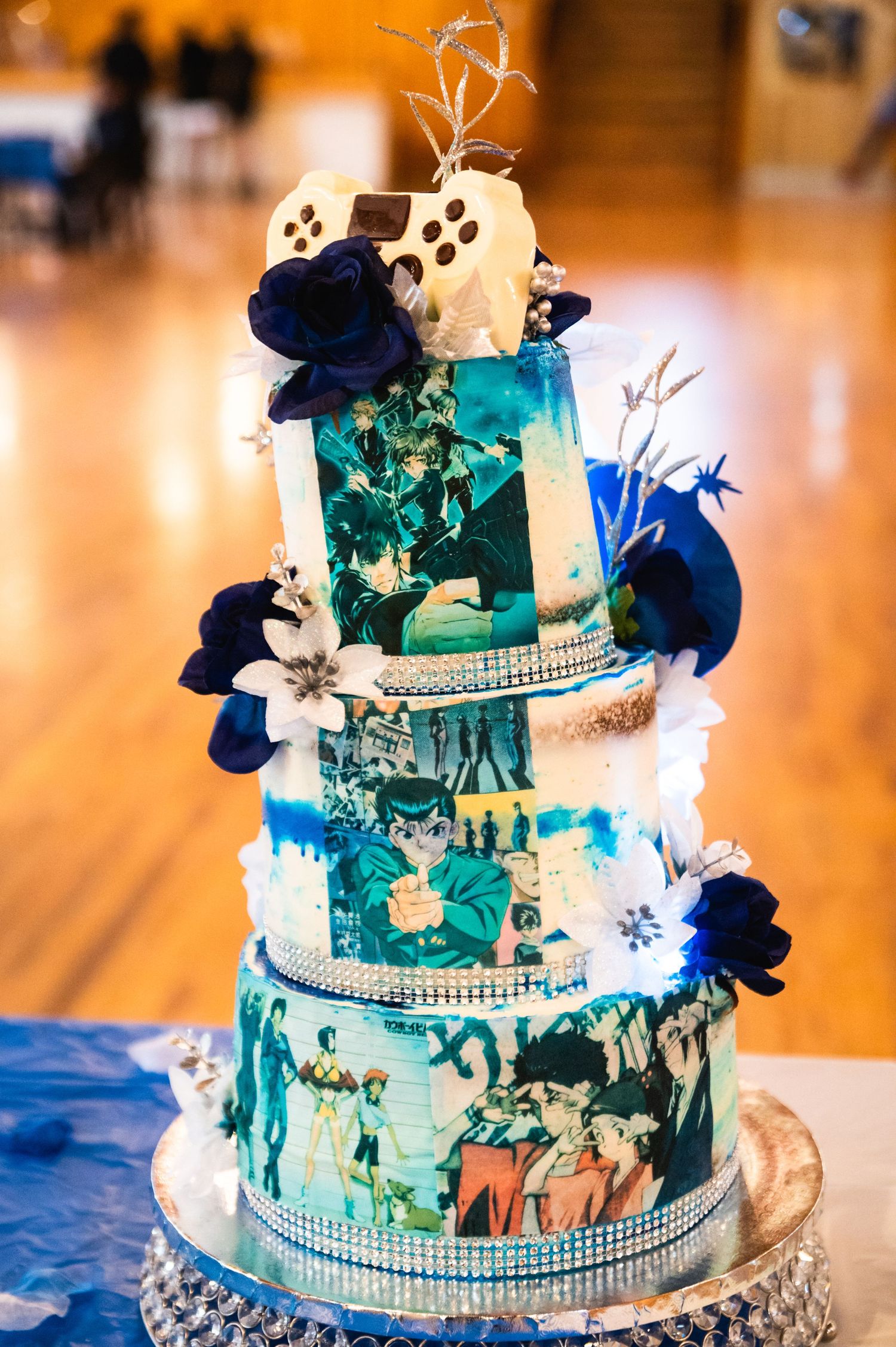 Elegant tiered wedding cake decorated with blue flowers and rhinestone trim in teal and white colors.