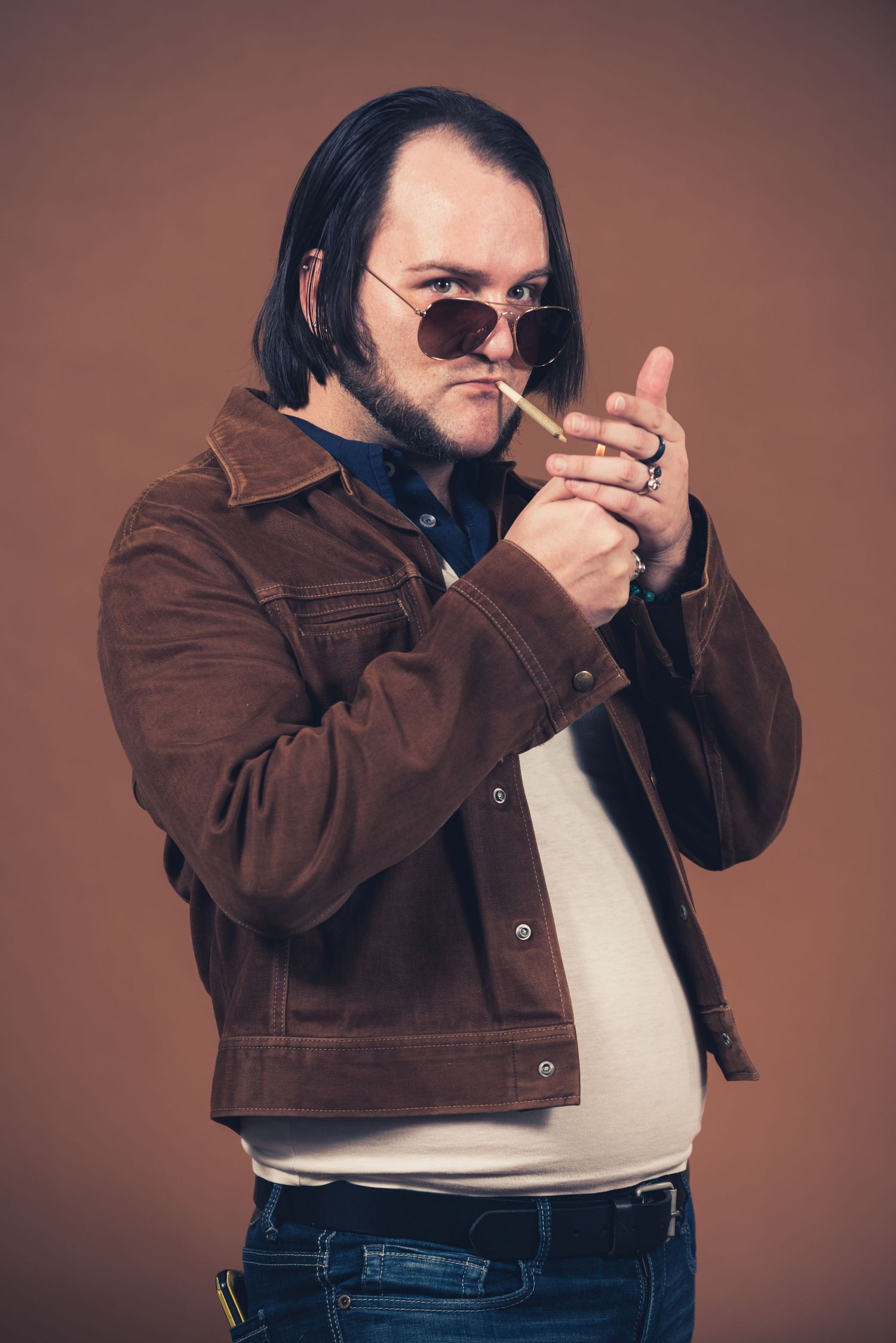 Person in brown jacket and sunglasses lighting up against brown background.