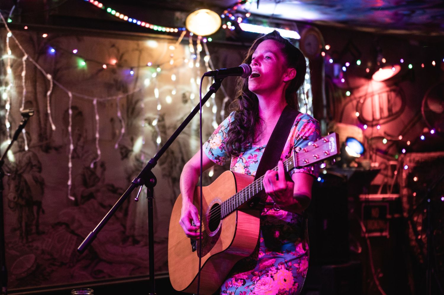 Acoustic guitarist performs on intimate stage decorated with string lights.