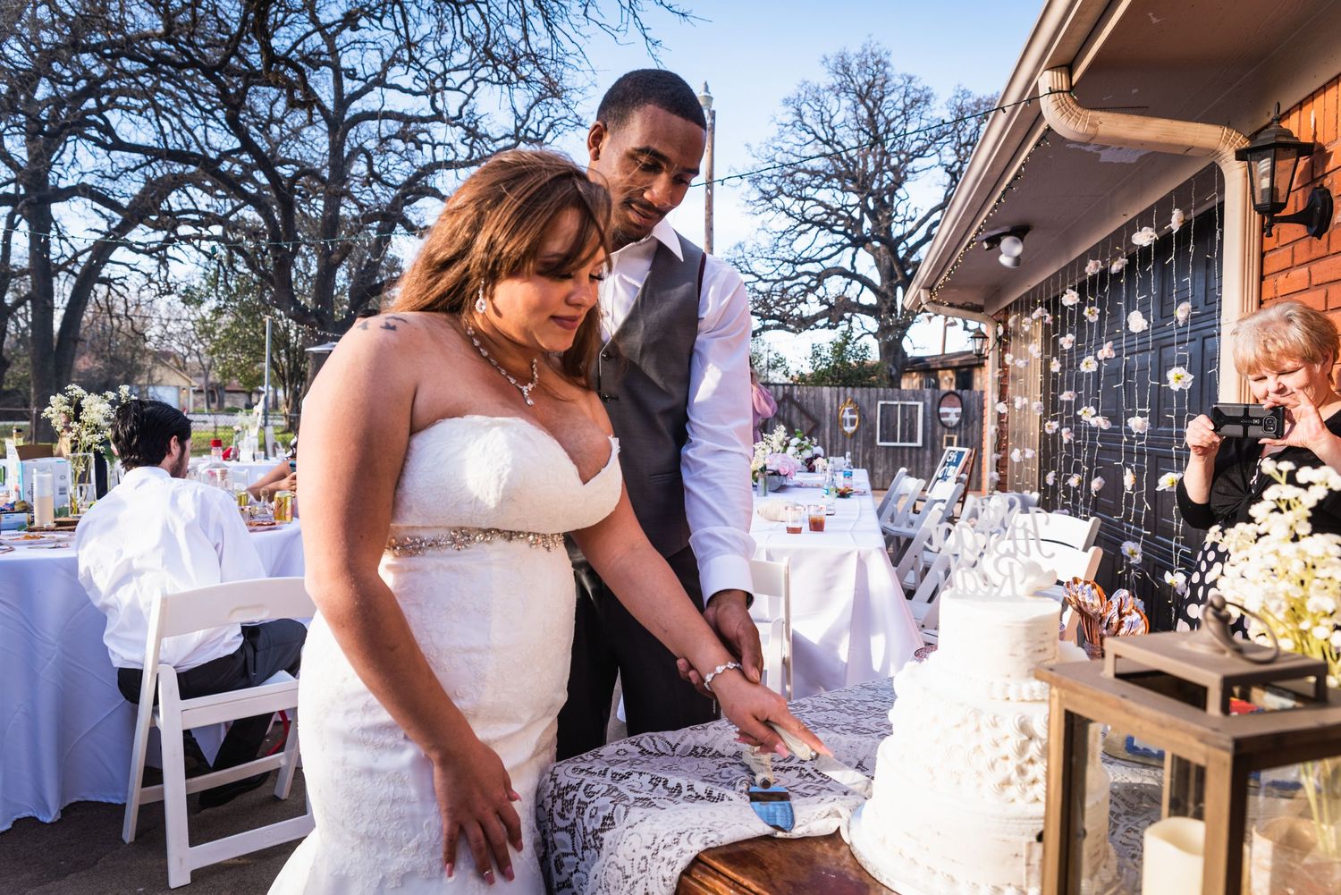 A couple shares an intimate moment while cutting their wedding cake at an outdoor reception.