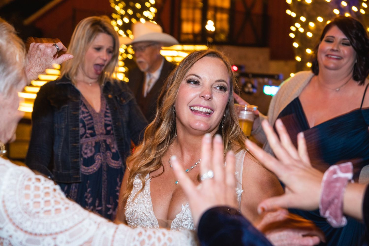 A bride celebrates with friends on the dance floor with energetic expressions and raised hands.