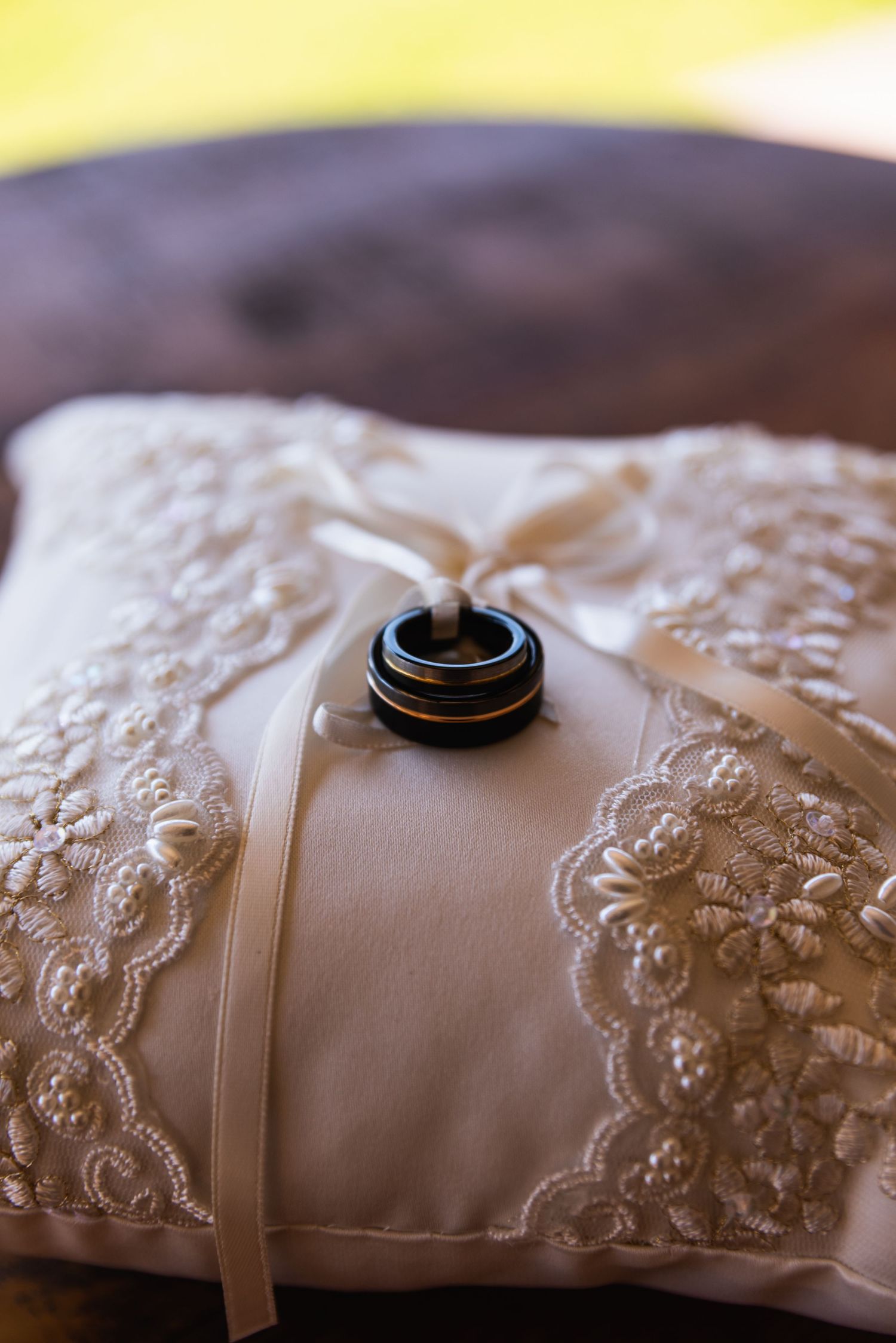 Wedding rings rest on a white lace pillow with intricate embroidery details.