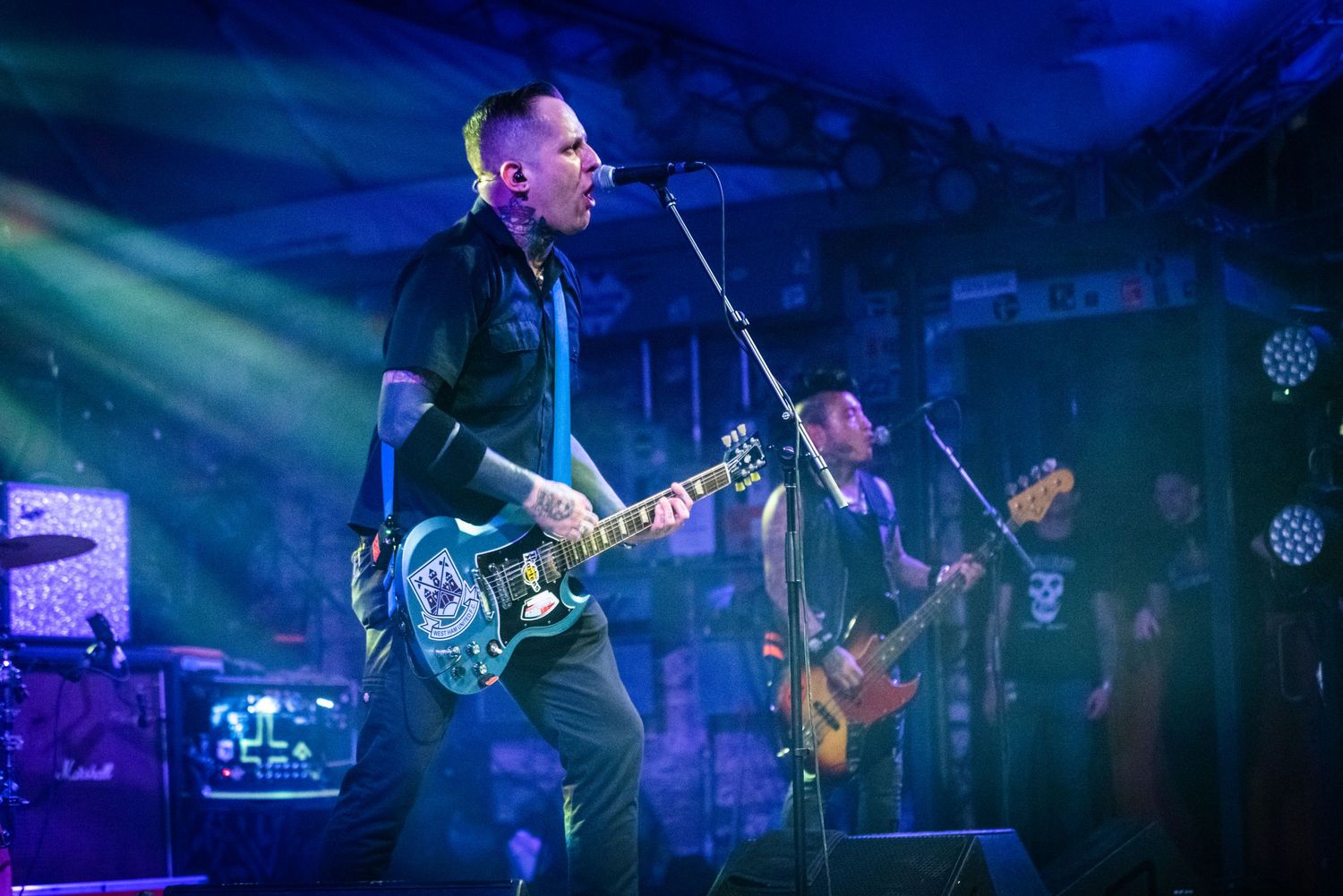 Musician performing with electric guitar under blue stage lighting at concert venue.
