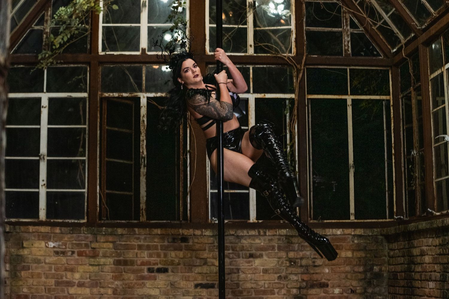 Athletic pole dance performance in front of vintage greenhouse windows.
