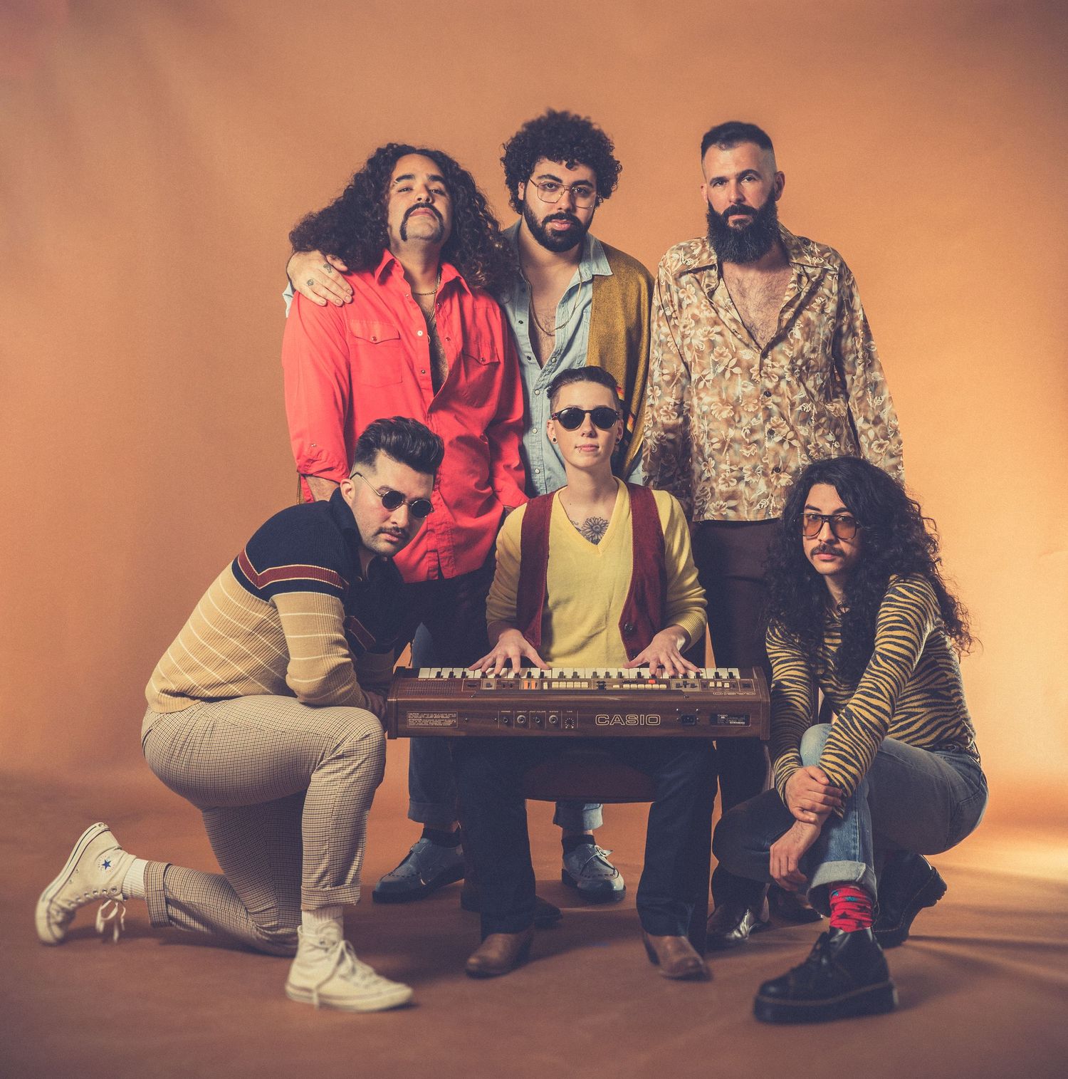 Group photo of band members posing around a keyboard against orange background.