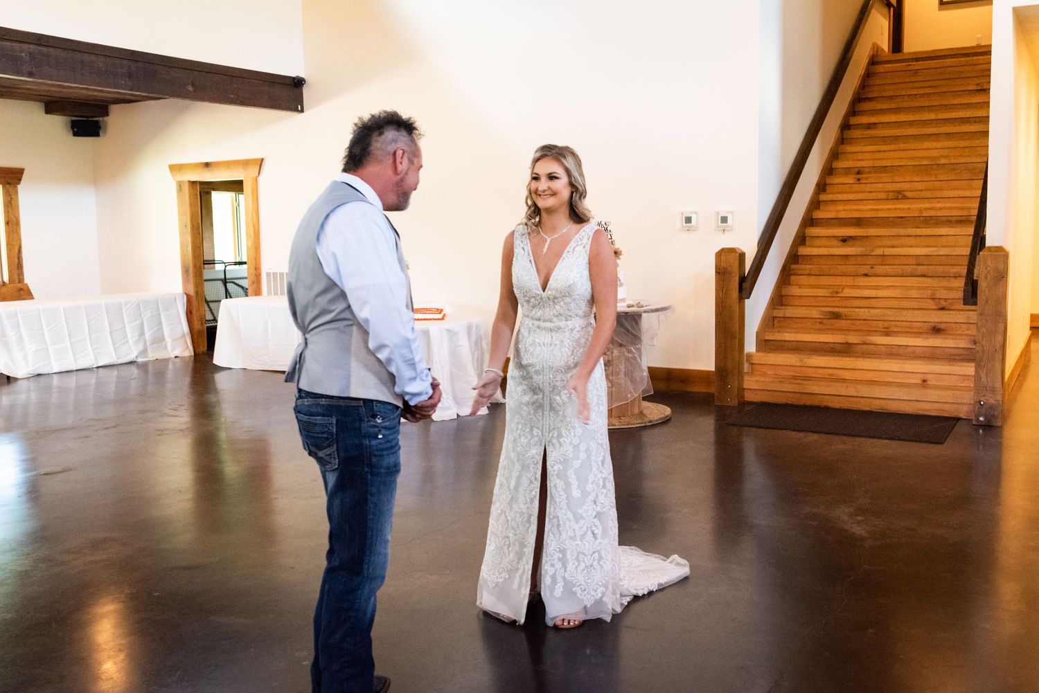 A heartfelt first look moment between newlyweds in a rustic indoor venue with wooden stairs and white walls.