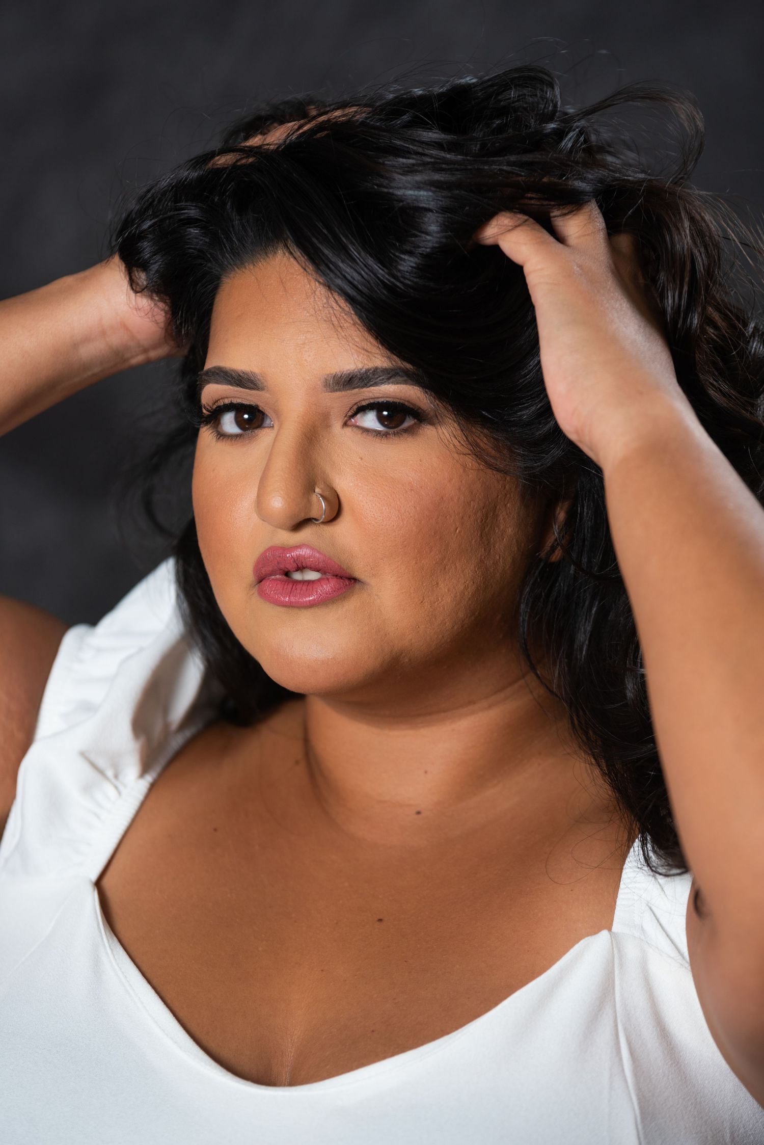 Lifestyle portrait showing natural beauty with hands in hair against dark backdrop.