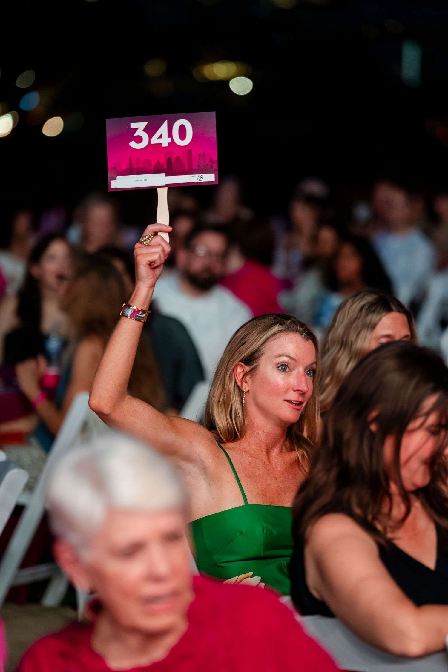 People holding up numbered auction paddles at an event with colorful lighting in the background.