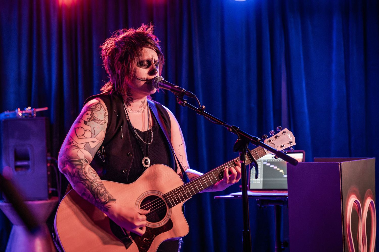 Musicians perform on stage with acoustic guitars under dramatic blue and red stage lighting during a live concert.