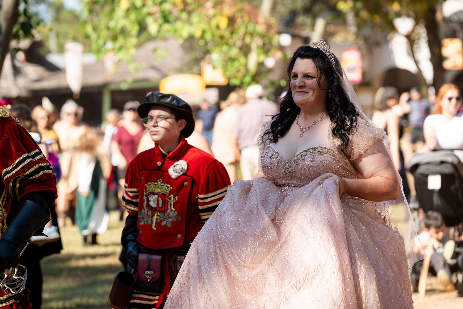 A wedding party celebrates outdoors on a sunny day with guests in traditional red uniforms and formal attire.