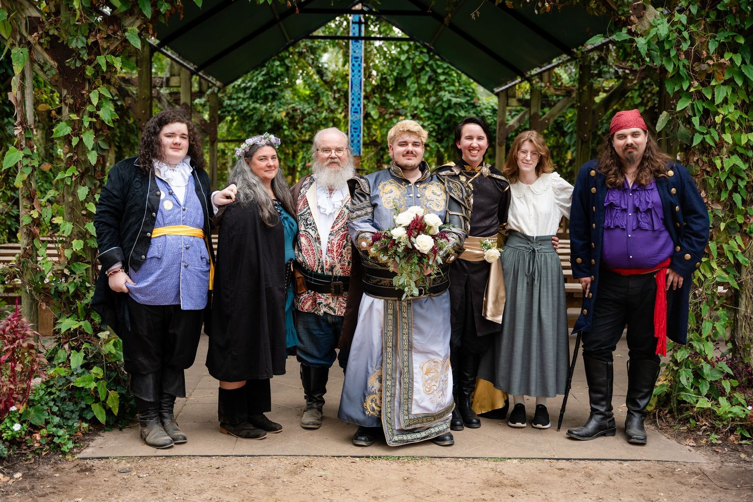 A wedding party poses together in a lush garden setting with greenery and flowers in the background.