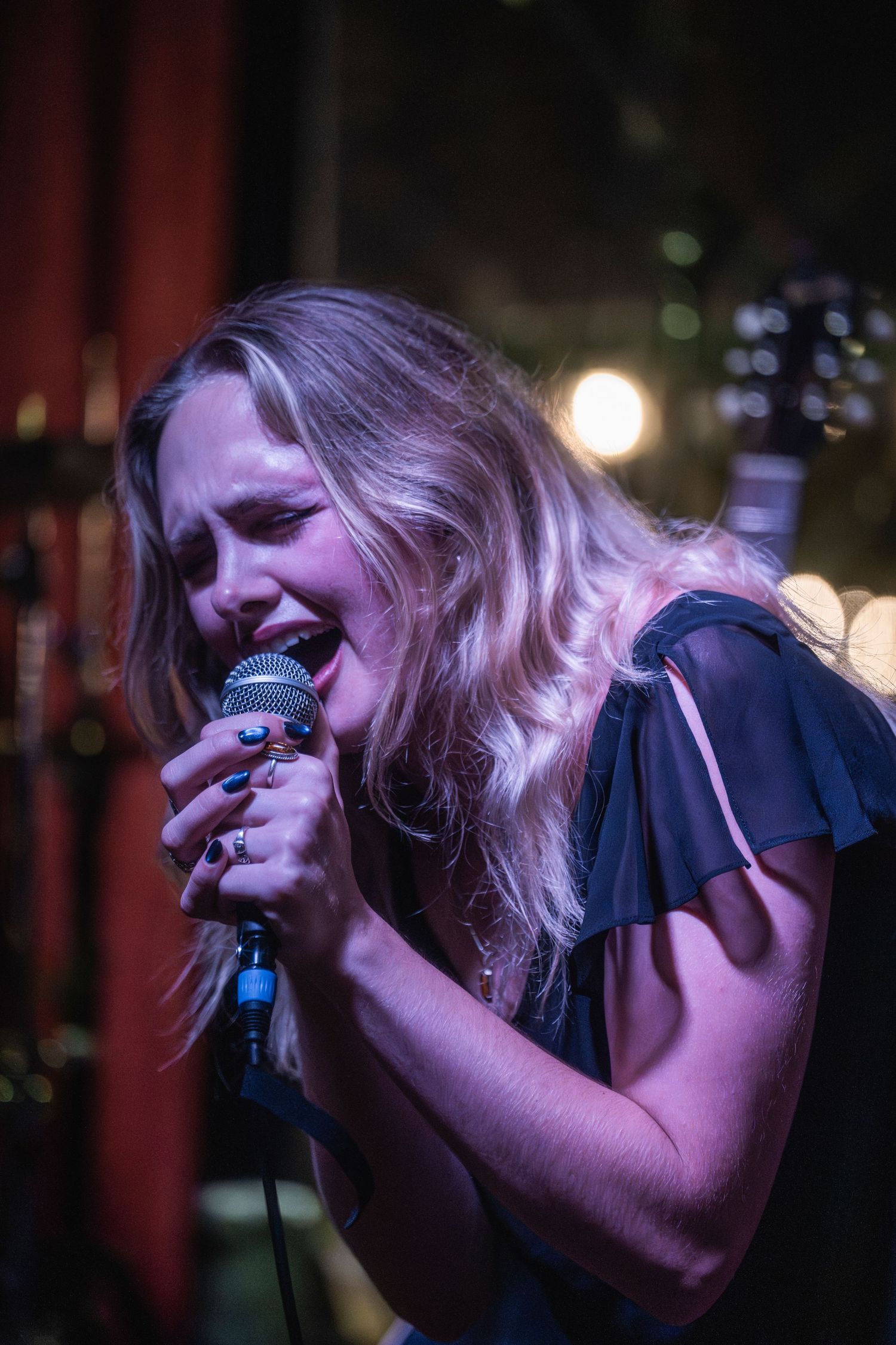A passionate singer performs with intense emotion at a dimly lit venue, leaning into the microphone during their performance.