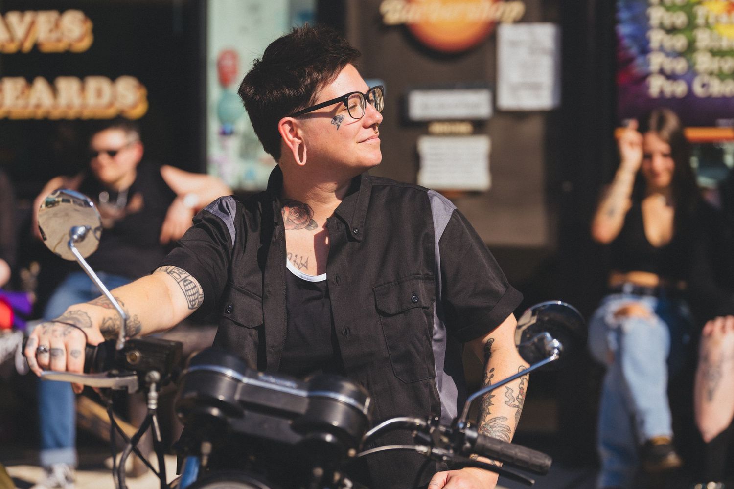 A person in black clothing rides a bicycle through a busy city street with shops and pedestrians in the background.