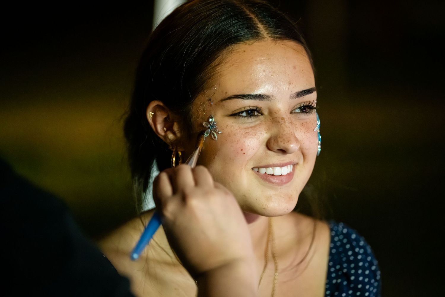 Someone getting makeup applied with a blue brush while smiling during a beauty preparation session.