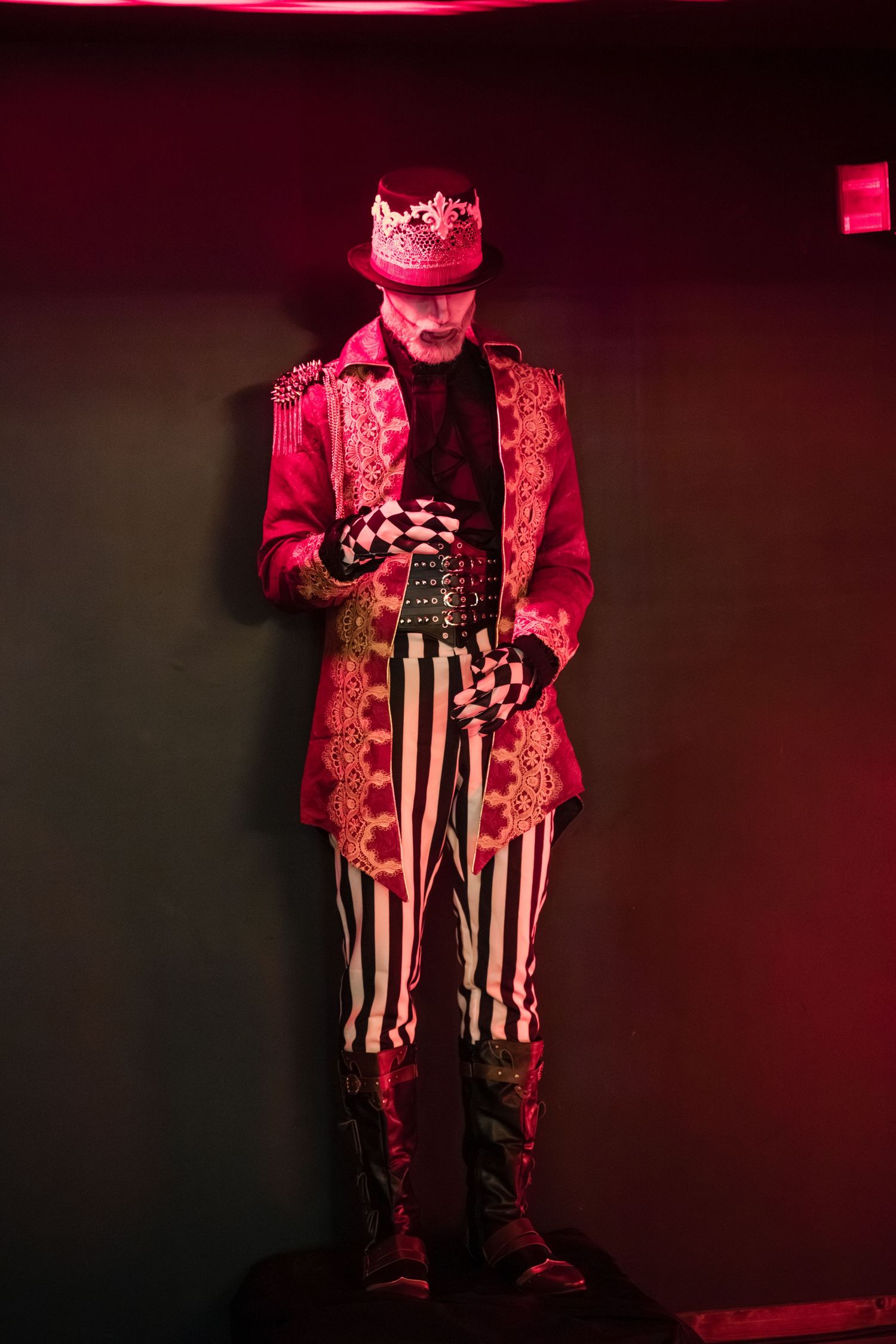 Figure in red lighting wearing striped pants and jacket performs on darkened stage during theatrical performance.