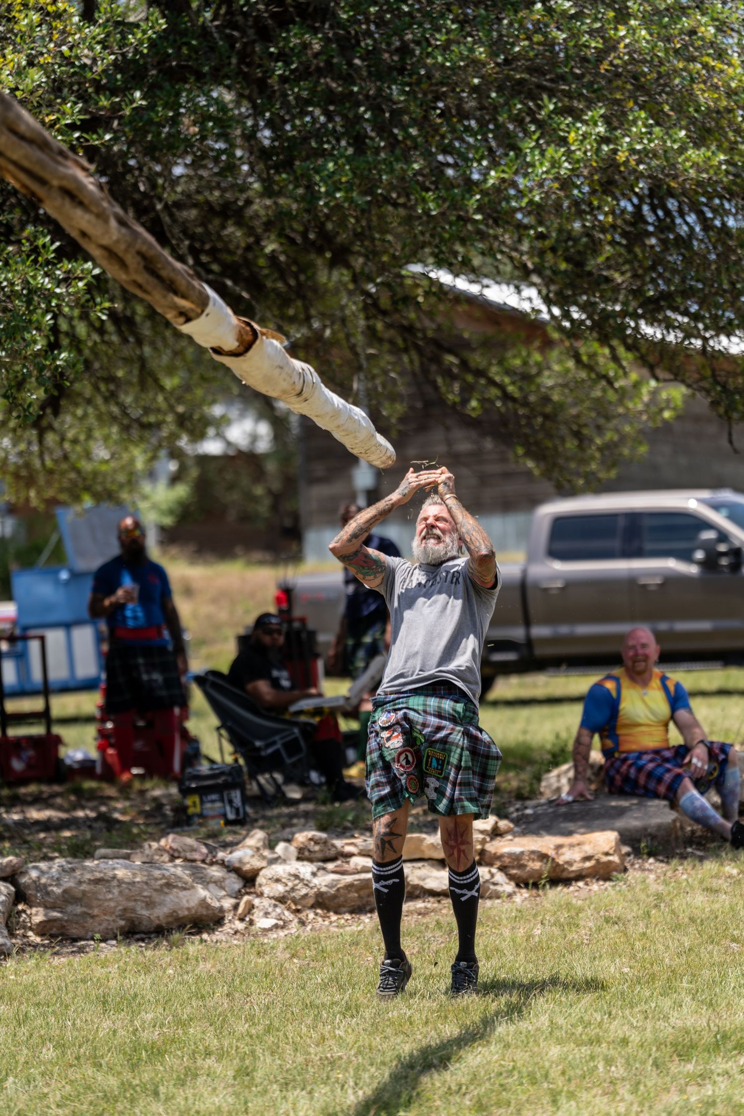 Man in tartan kilt tossing a caber at a Highland Games competition outdoors.