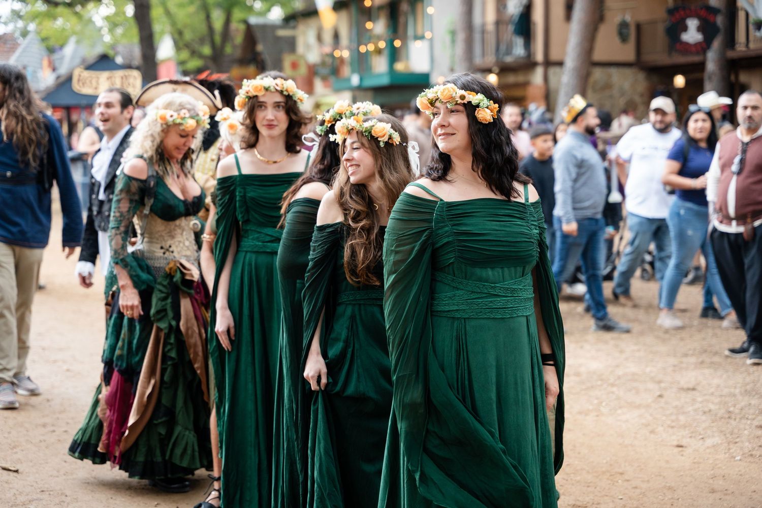 Group wearing matching emerald green velvet renaissance dresses with flower crowns at a medieval festival.