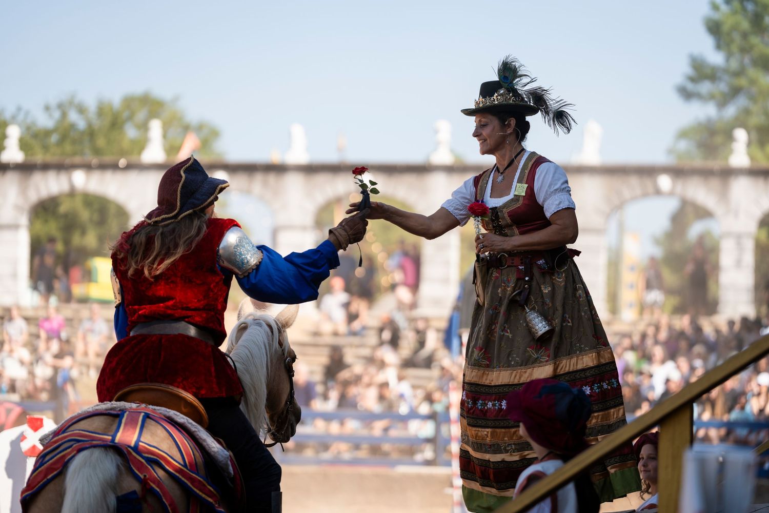 Two performers in traditional medieval costumes engage in a staged combat scene at a renaissance festival.