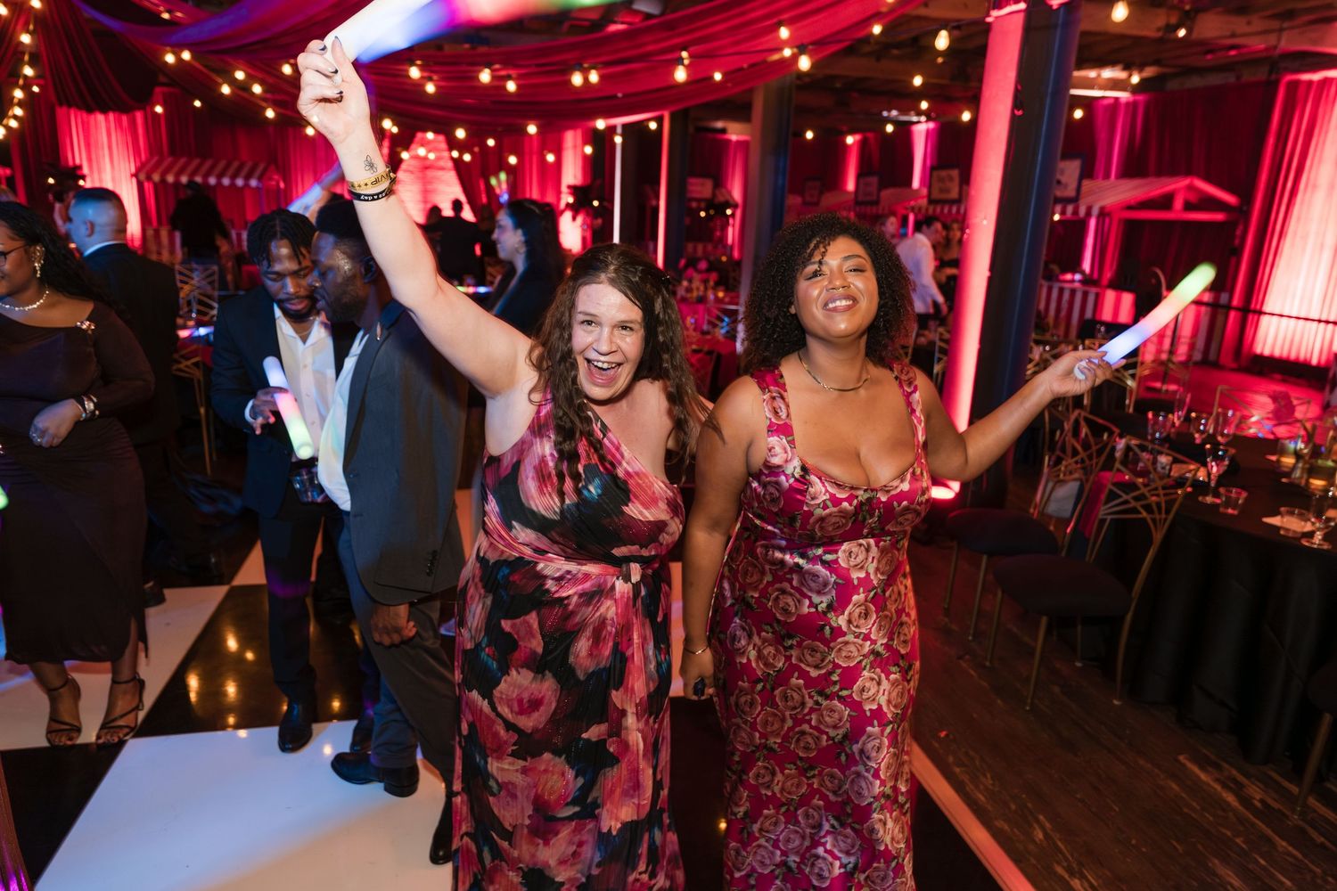 People dancing and celebrating at a nightclub with red lighting and festive atmosphere.