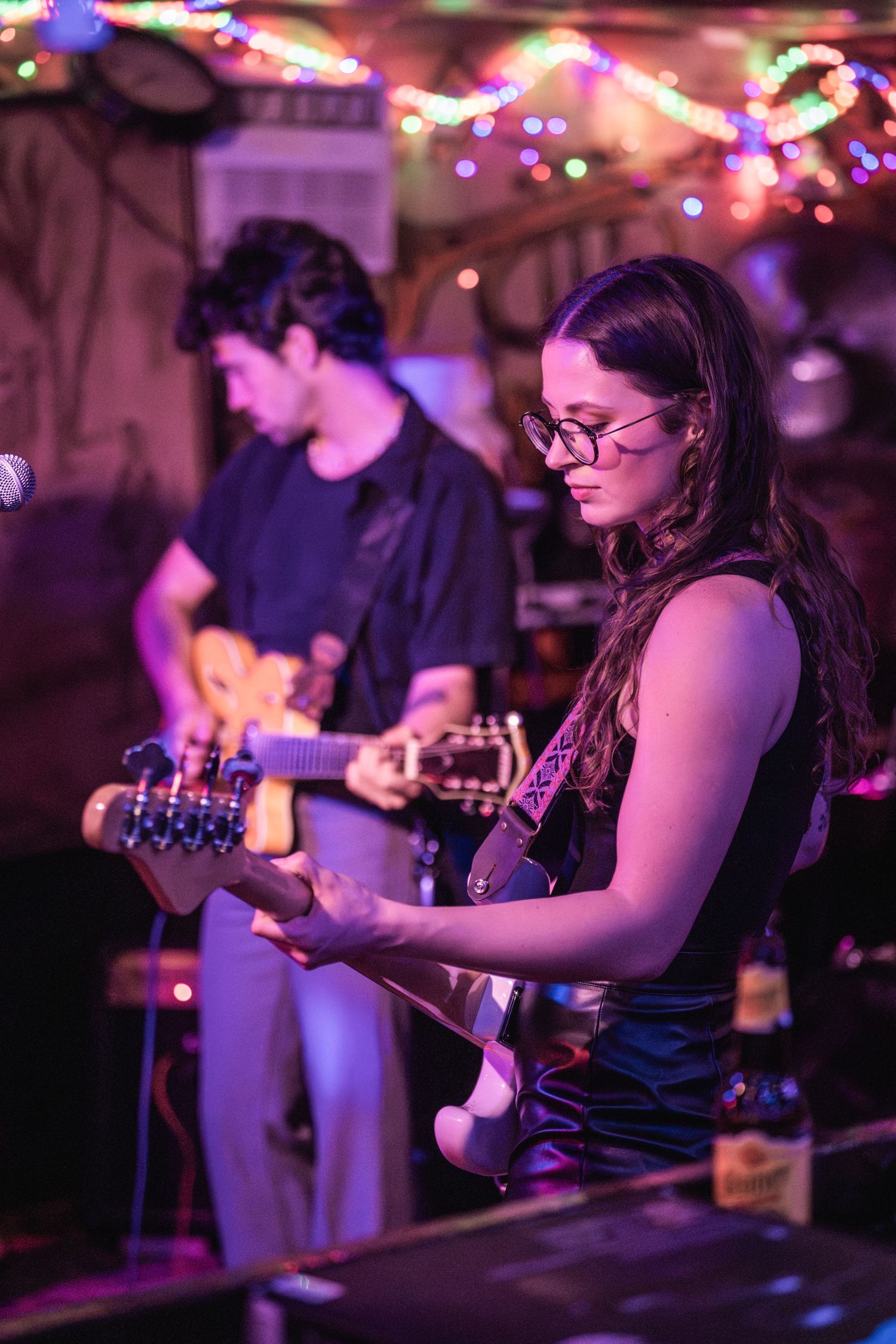 Musicians perform on stage in a dimly lit venue with purple lighting and string instruments.