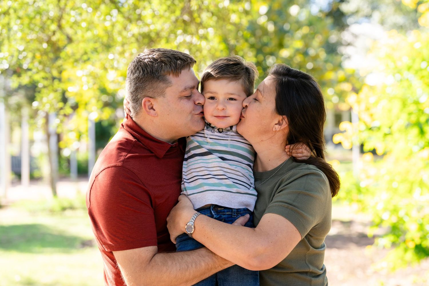 A family shares tender moments together in a sunny outdoor setting with golden autumn foliage in the background.