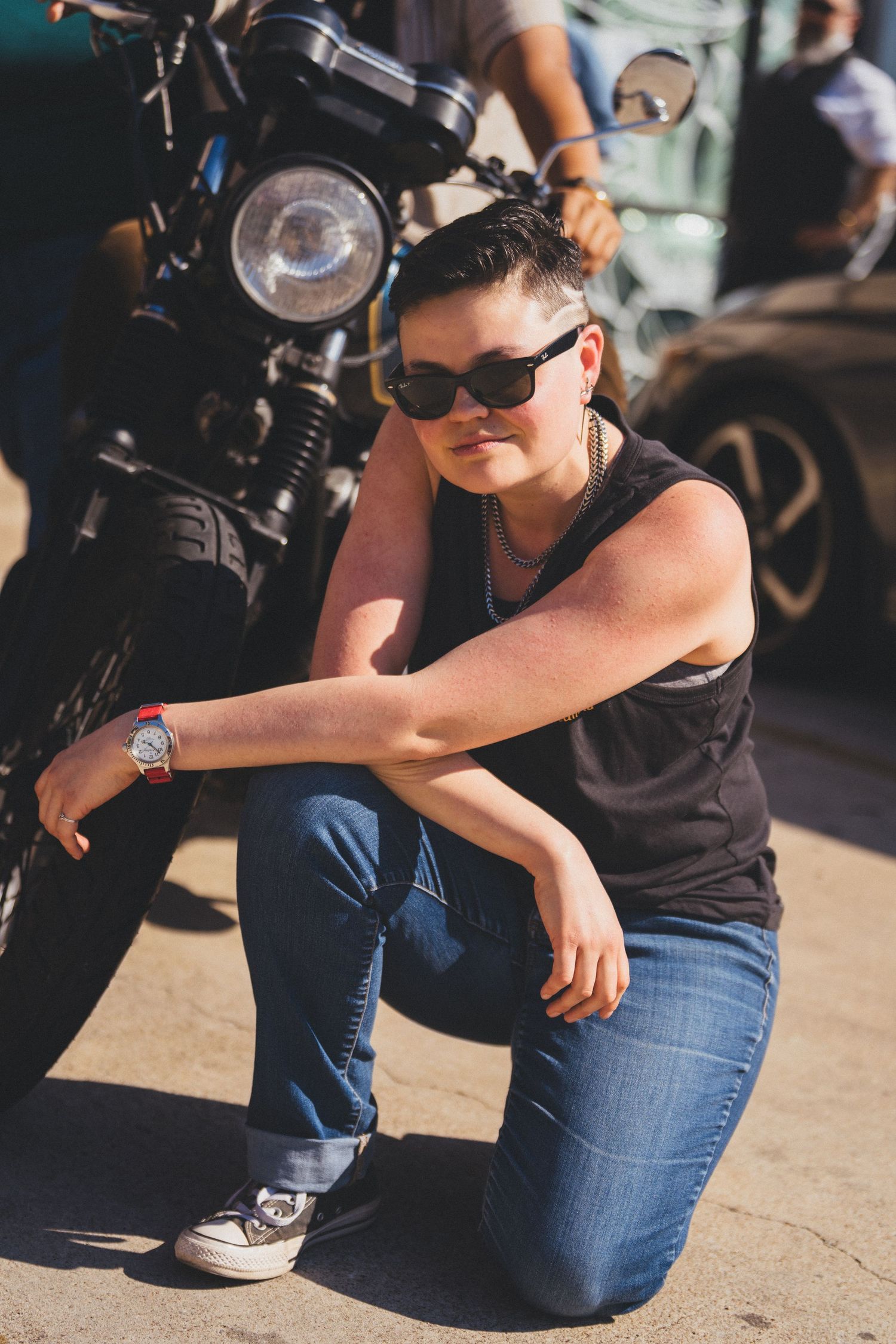 A photographer in black shirt and jeans crouches low to capture a shot with a professional camera in natural lighting.
