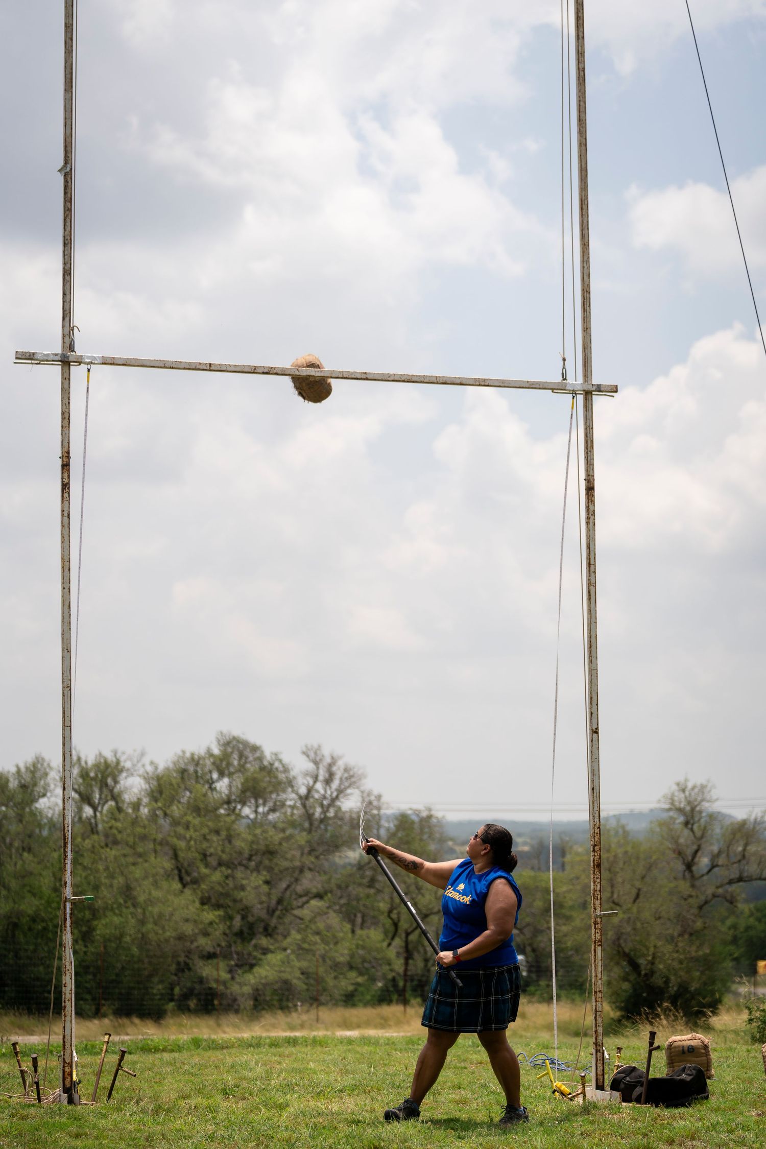 Athlete performs hammer throw sequence in grassy field with poles and equipment visible in background.