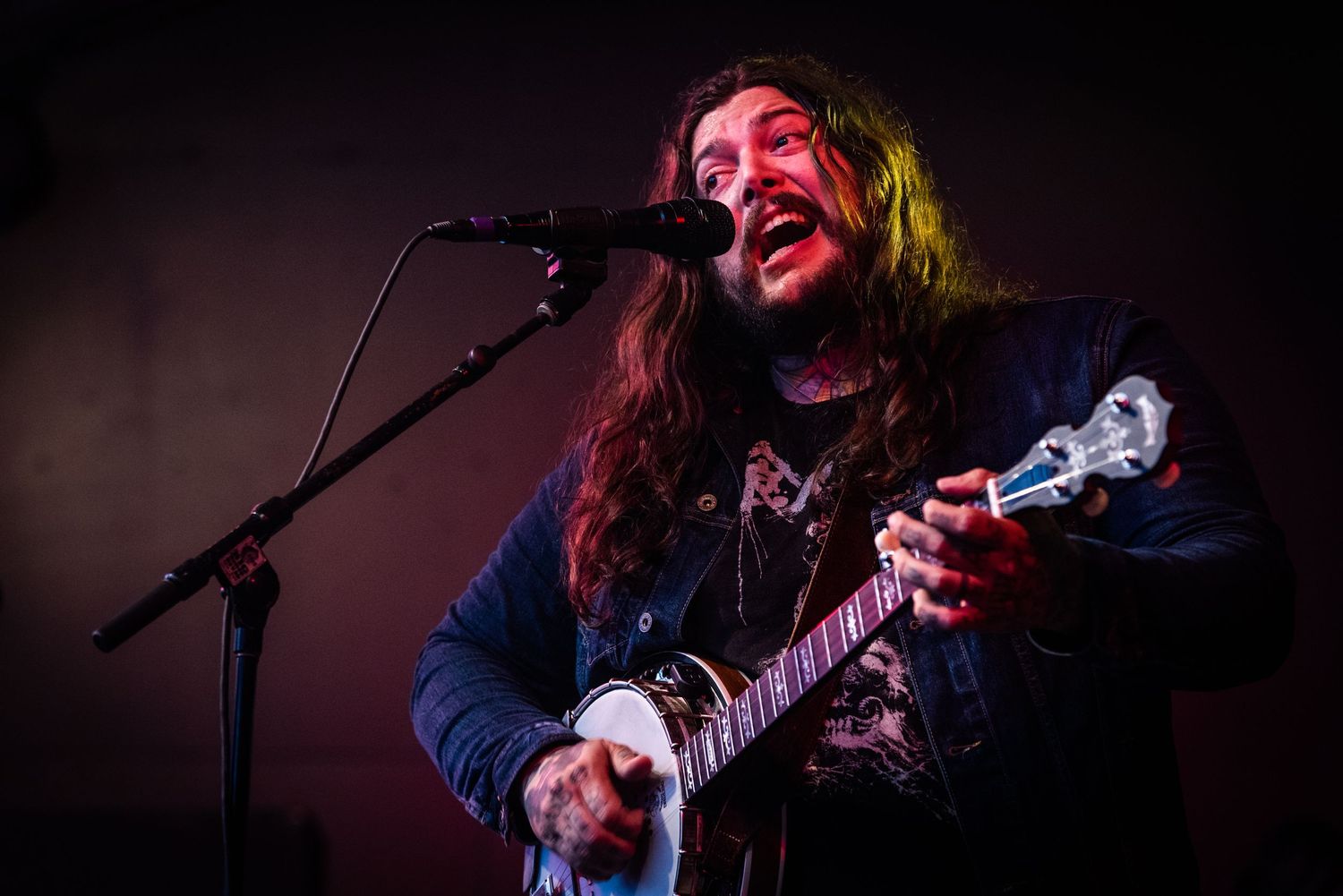 A musician performs on stage with a guitar and microphone, illuminated by dramatic red and yellow lighting.